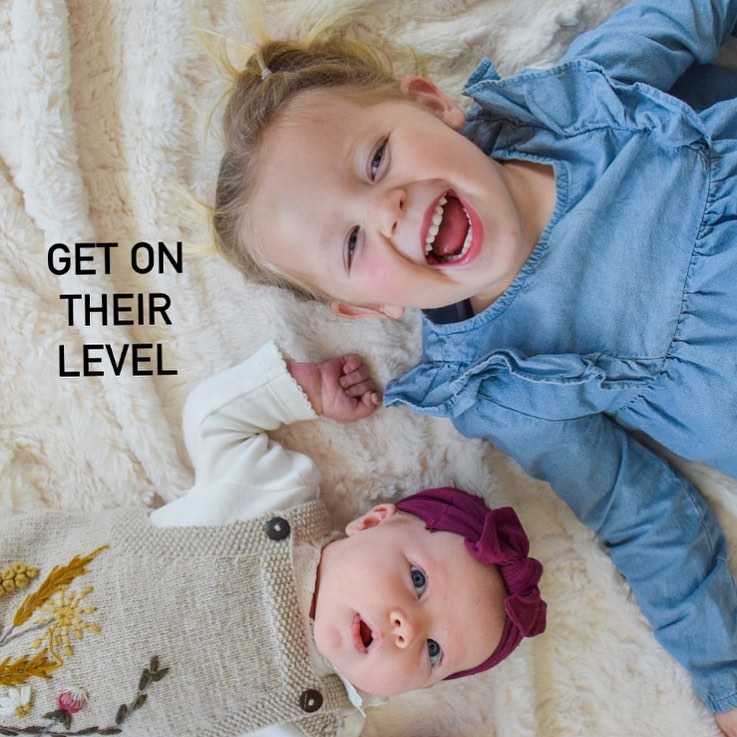 Two young children laughing on a soft blanket with the words Get On Their Level