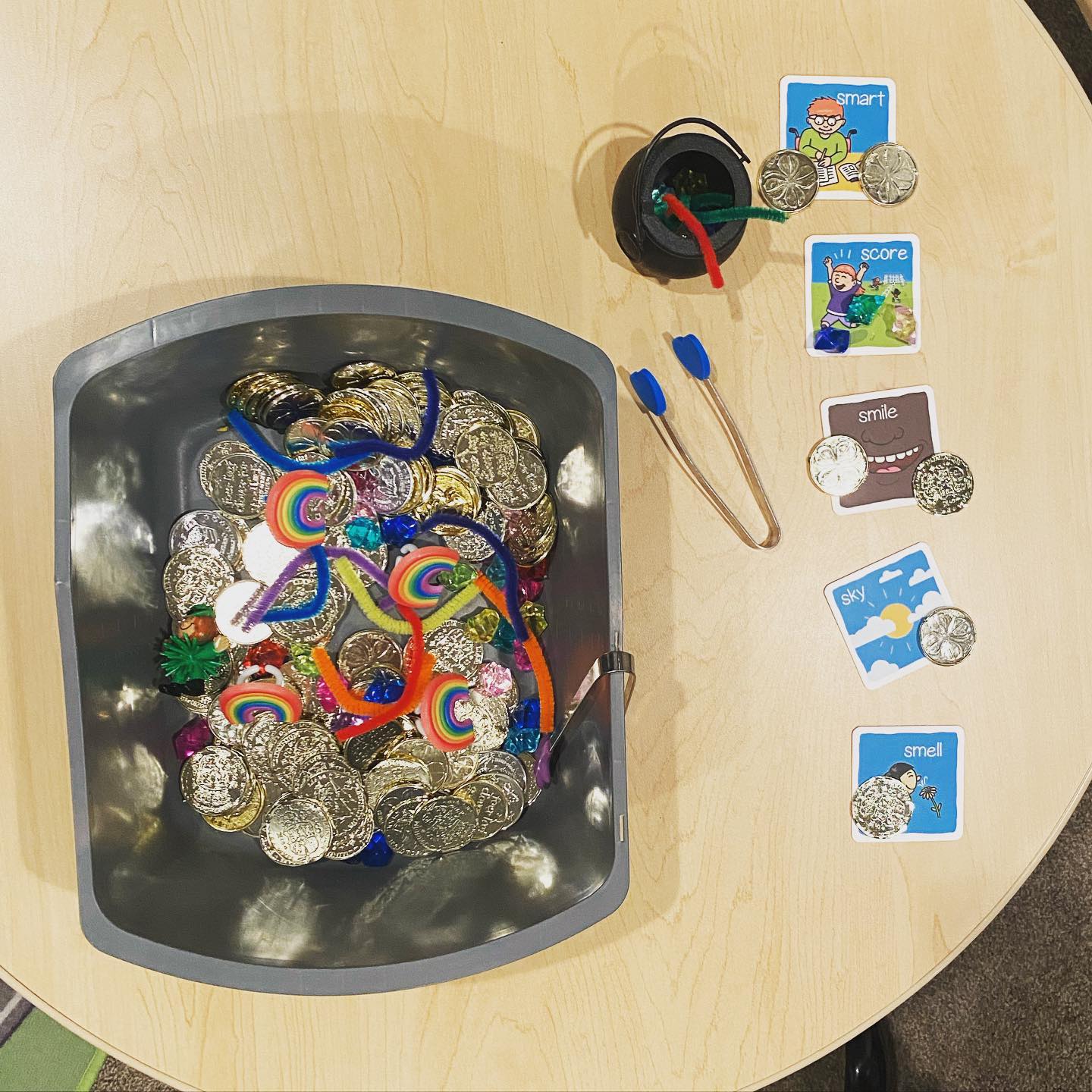 Speech therapy sensory bin with gold coins, tongs, and picture word cards.